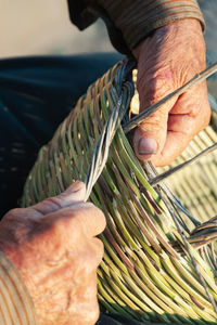 Unrecognizable elderly craftsman making authentic wicker basket on sunny day