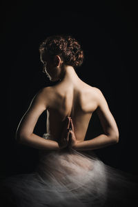 Rear view of topless woman doing hands clasped against black background