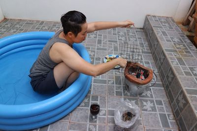 High angle view of woman preparing food on stove while sitting in inflatable pool