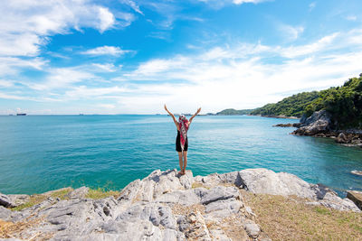 Man standing on rocks by sea against sky