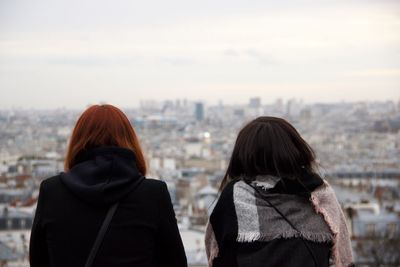 Rear view of women looking at cityscape against sky