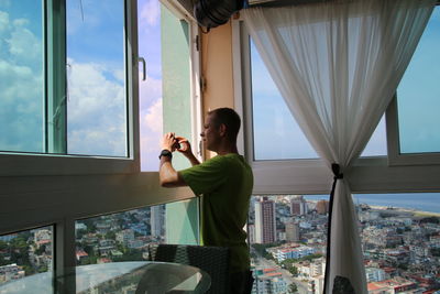 Man holding mobile phone while standing by window at home