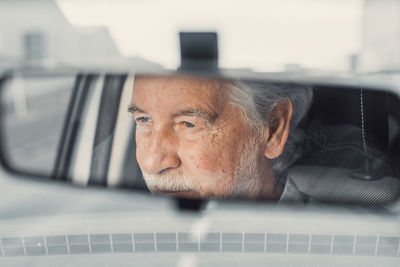 Reflection of smiling senior man sitting in car