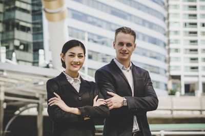 Portrait of business people with arms crossed standing against building in city