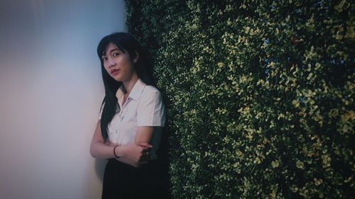 Portrait of young woman standing against plants