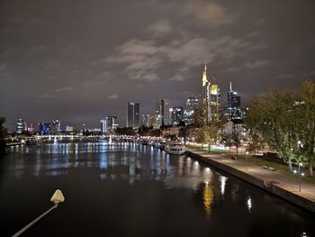 Illuminated buildings by river against sky in city at night