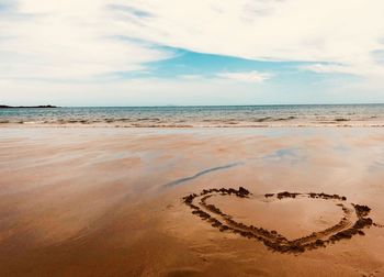 Heart shape on sand at beach against sky