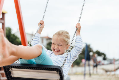 Cheerful girl on swing at playground against sky