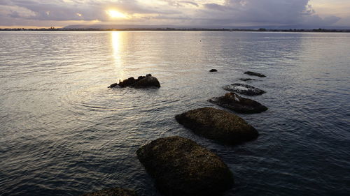 Rocks in sea against sky during sunset