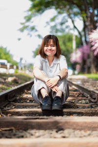 Portrait of a smiling young woman sitting on railroad track