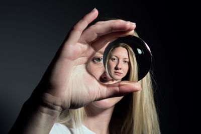 Close-up portrait of woman holding crystal ball with reflection against black background