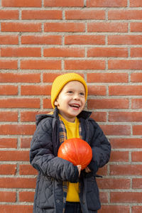 Boy with a pumpkin in his hands against a brick wall.
