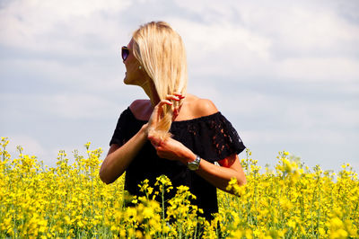 Smiling young woman with hand in hair standing on oilseed rape field