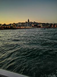 Sea by buildings against clear sky during sunset