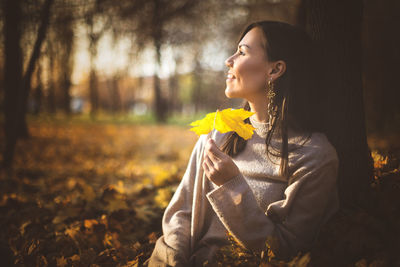 Smiling woman looking away holding leaf during autumn