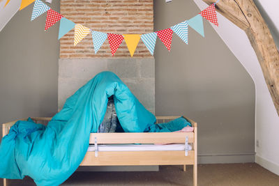 Child hiding under blanket on bed