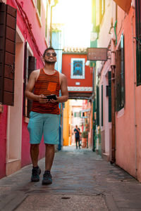 Full length portrait of young man walking in alley amidst buildings