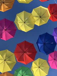 Low angle view of multi colored umbrellas hanging against blue sky
