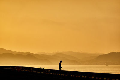 Silhouette man standing on beach against orange sky