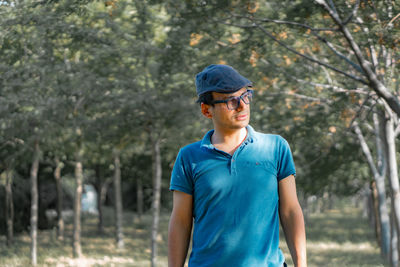 Mature man wearing cap and eyeglasses standing against trees in forest