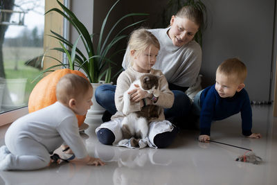 Mother with her three children playing with a cat on the floor at home