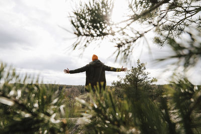 Rear view of man standing arms outstretched on sunny day