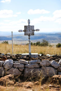 Tombstone at war memorial by fence against cloudy sky