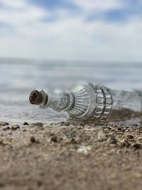 Glass bottle washing up on shore with water and sky in the back