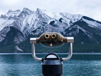 Coin-operated binoculars by snowcapped mountains against sky