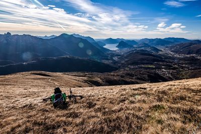 Rear view of man with backpack and bicycle sitting on mountain against sky