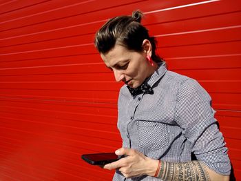 Young man using mobile phone against red wall