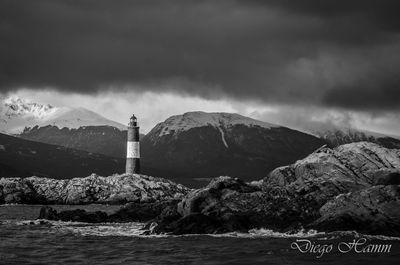 Lighthouse by sea against mountain and sky