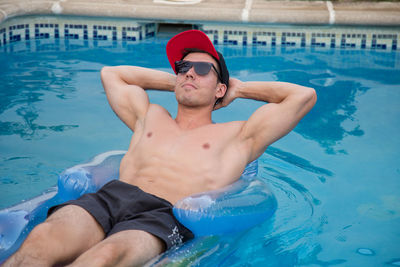 Shirtless young man relaxing on pool raft in swimming pool