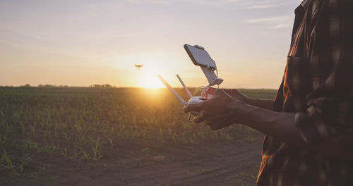 Man holding umbrella on field against sky during sunset