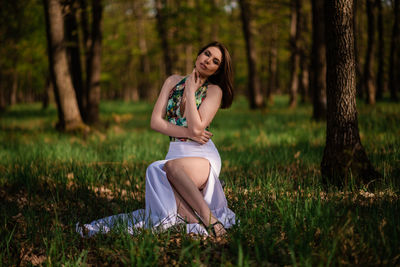 Portrait of woman sitting on tree trunk in field