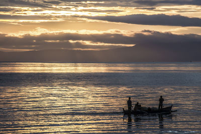Silhouette people on sea against sky during sunset