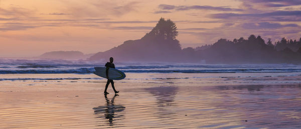 Rear view of woman standing at beach against sky during sunset