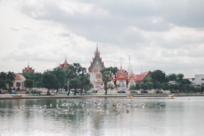 View of buildings by river against cloudy sky