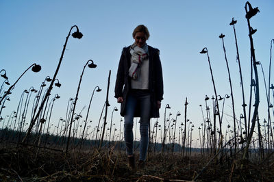 Woman walking on field with wilted flowers against sky