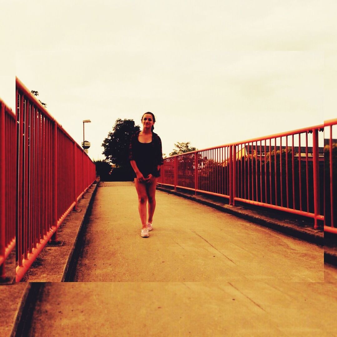 full length, lifestyles, casual clothing, young adult, railing, architecture, built structure, leisure activity, the way forward, walking, standing, clear sky, person, young women, bridge - man made structure, connection, rear view, front view