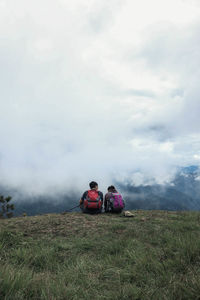 People sitting on land against cloudy sky