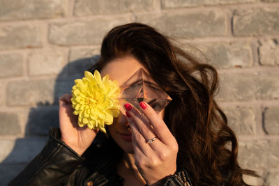 Portrait of woman holding yellow flower and crystal against wall