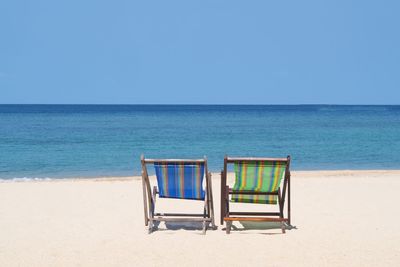 Deck chairs at beach against clear blue sky