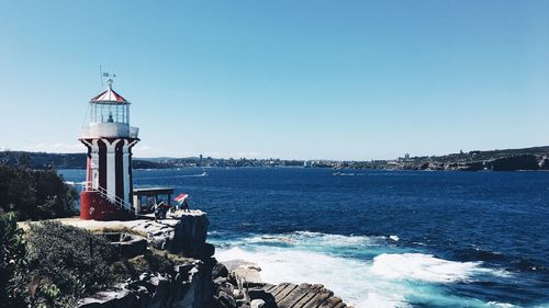 Lighthouse by sea against clear sky