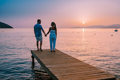 Rear view of friends standing on sea against sky during sunset