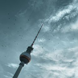 Low angle view of communications tower against cloudy sky