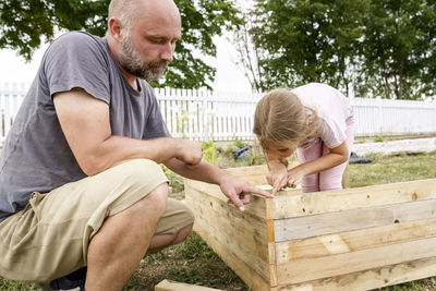 Father teaching daughter to measure wooden raised bed in back yard