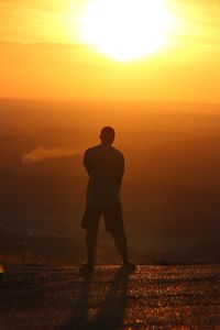 Silhouette man standing on landscape against orange sky
