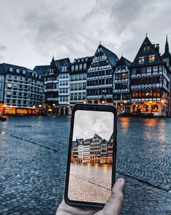 Person holding umbrella by river against buildings in city