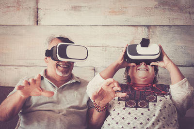 Smiling couple wearing virtual reality simulator while sitting at home